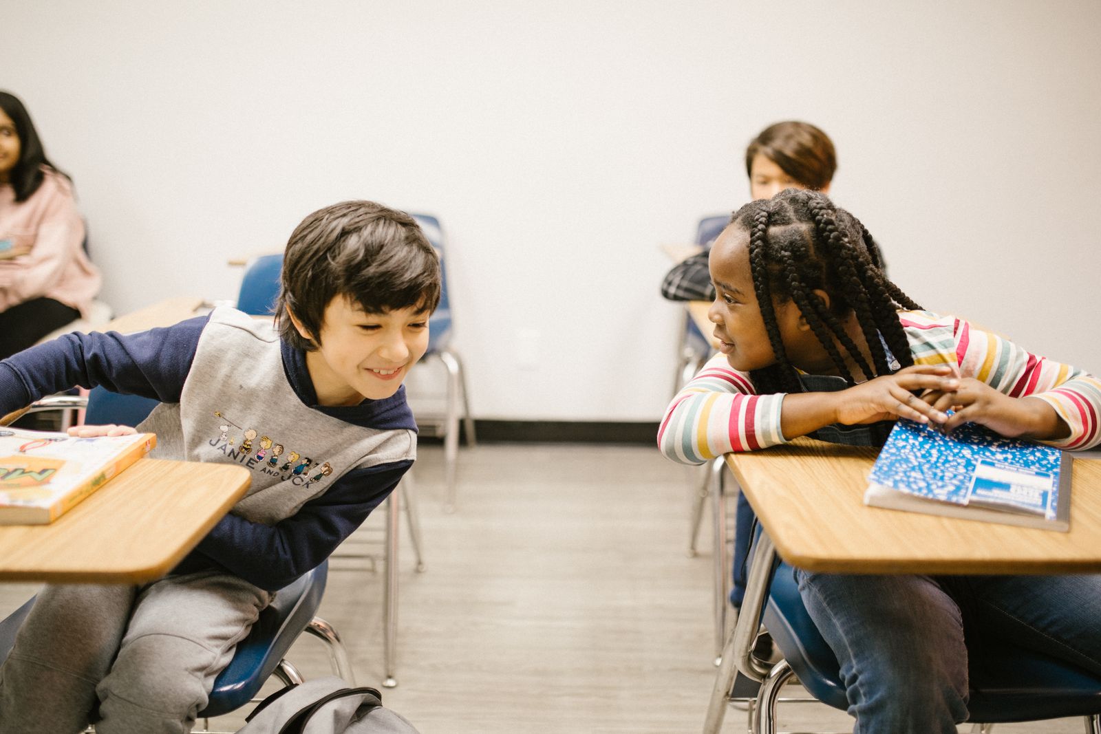 Two elementary-aged students leaning across their desks to talk together